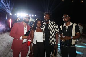 Four friends pose together smiling at an outdoor night event, dressed in stylish outfits including a red blazer.
