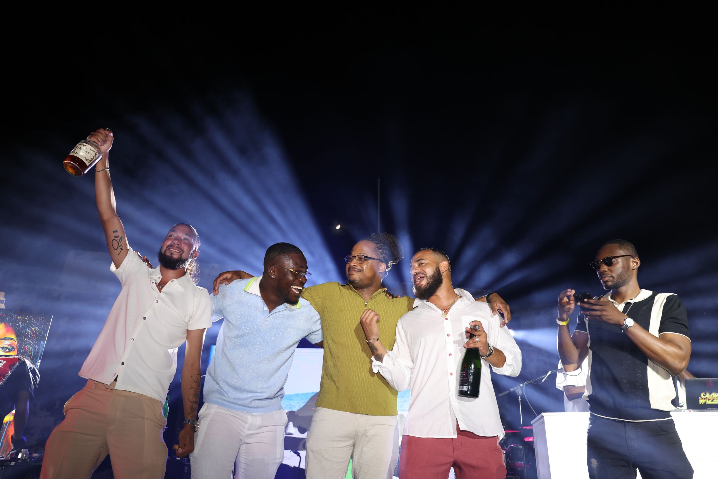 Group of men celebrating with trophy and champagne at outdoor night event.