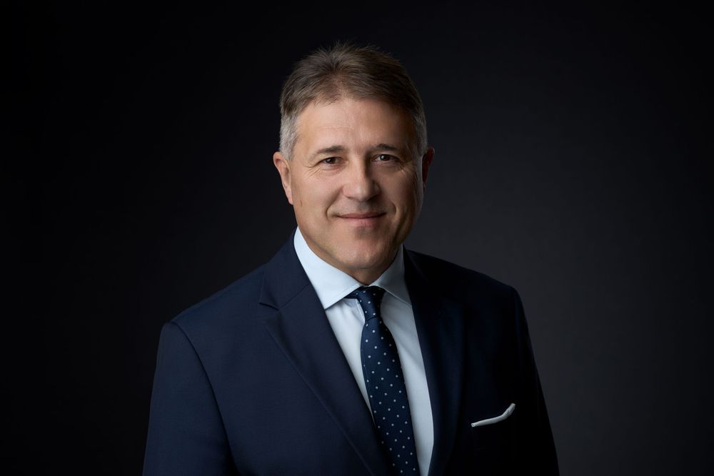 Professional businessman in navy suit and tie posing confidently against dark studio background.