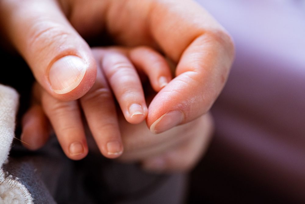 Klein babyhandje in moeders hand - Newborn lifestyle reportage aan huis - MaxFotos