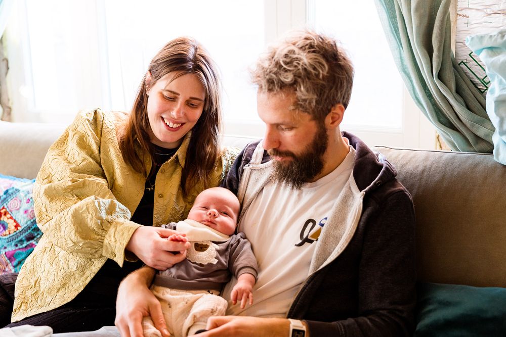 Ouders lachen gelukkig naar baby op de bank - new born lifestyle reportage aan huis - MaxFotos