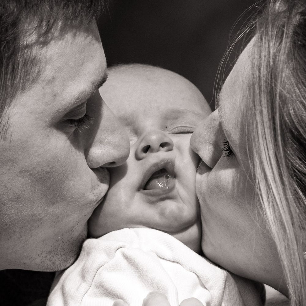 Zwart-wit New born lifestyle fotografie - kusje van papa en mama op de wangen van baby - Sonse vennen - MaxFotos