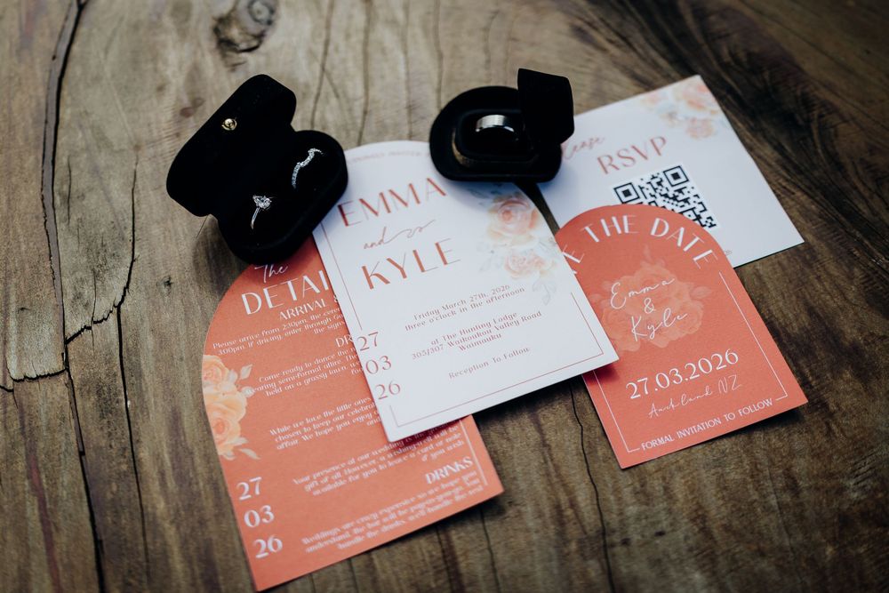 Coral wedding invitation suite with RSVP card, save the date, and detail card displayed with rings on rustic wood.