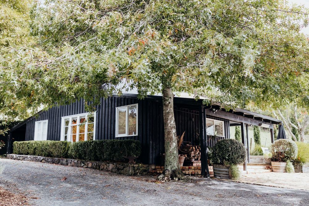 Black barn wedding venue surrounded by lush green trees on a sunny day.