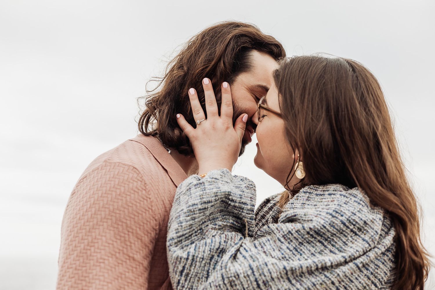 Romantic couple sharing a tender moment, almost kissing outdoors against a cloudy sky.