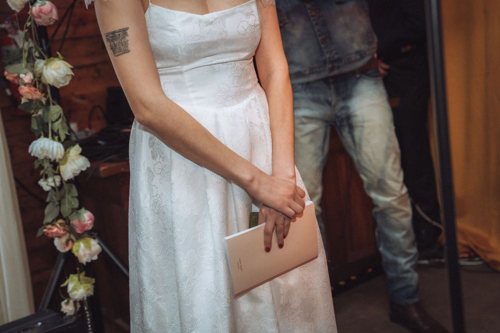 Bride in white strapless wedding gown holding a nude clutch purse beside floral arrangement.