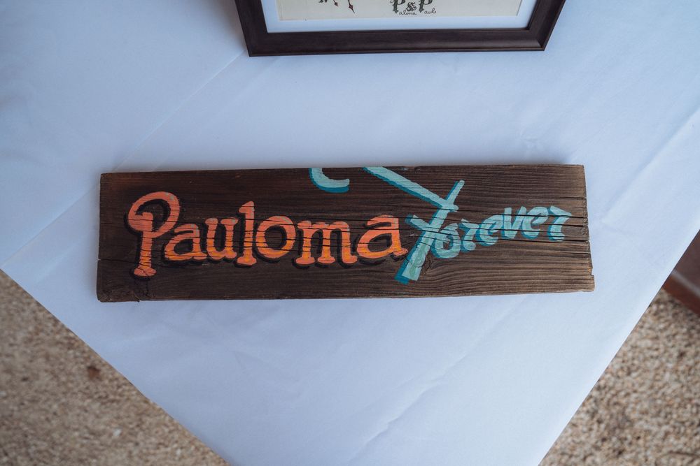 Wooden sign reading Pauloma Forever in colorful painted lettering displayed on a white tablecloth.