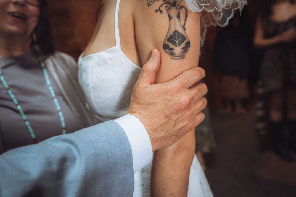 Close-up of a groom holding a tattooed bride's arm during a wedding ceremony.