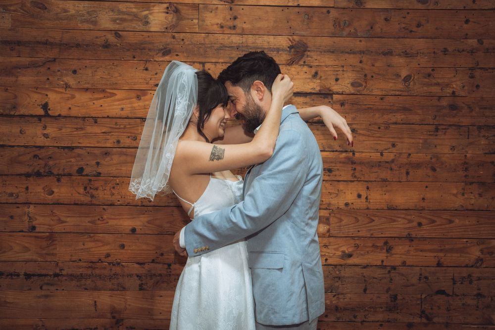 Bride and groom embracing tenderly in front of a rustic wooden wall on their wedding day.