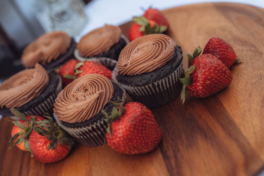 Chocolate cupcakes with rich chocolate frosting surrounded by fresh red strawberries on a wooden serving board.