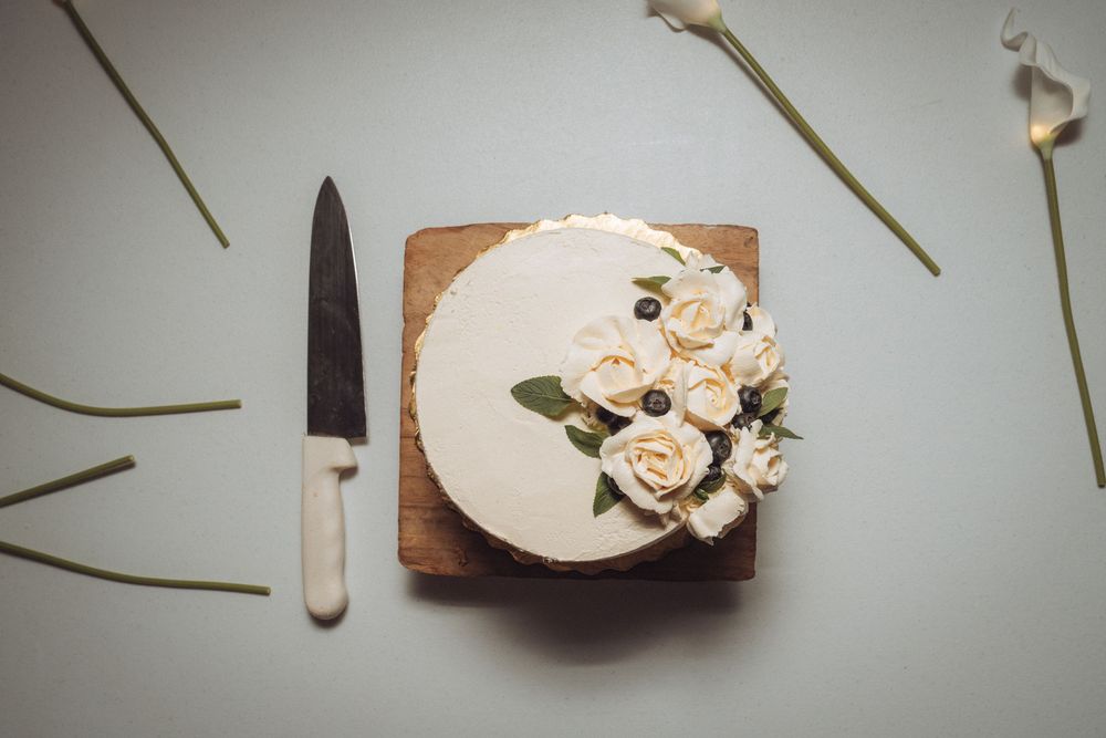 Elegant white frosted cake with cream roses on wood board, knife beside it on gray surface.