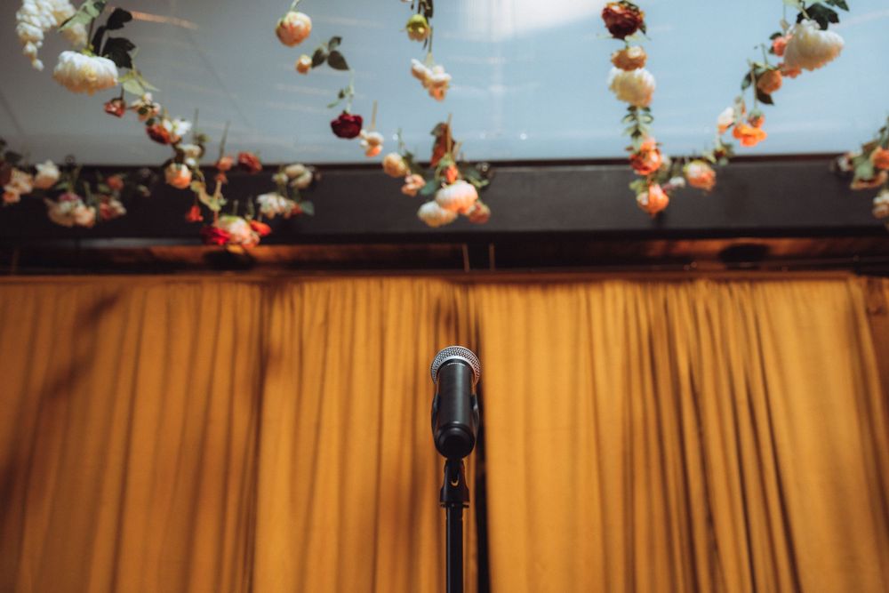 Vintage microphone on stage with golden curtains and floral garland decoration overhead.