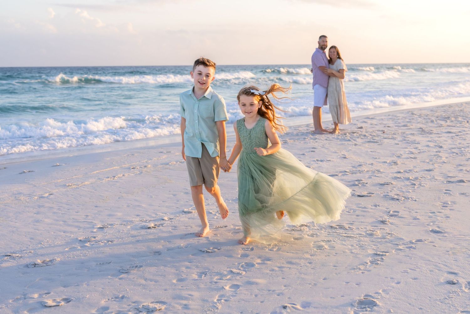 Young woman in blue sundress smiling on sandy beach at golden hour with pier in background.
