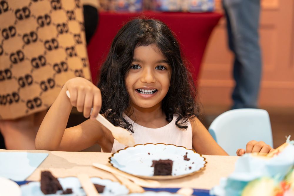 A young girl smiles while eating chocolate cake at a birthday party celebration.