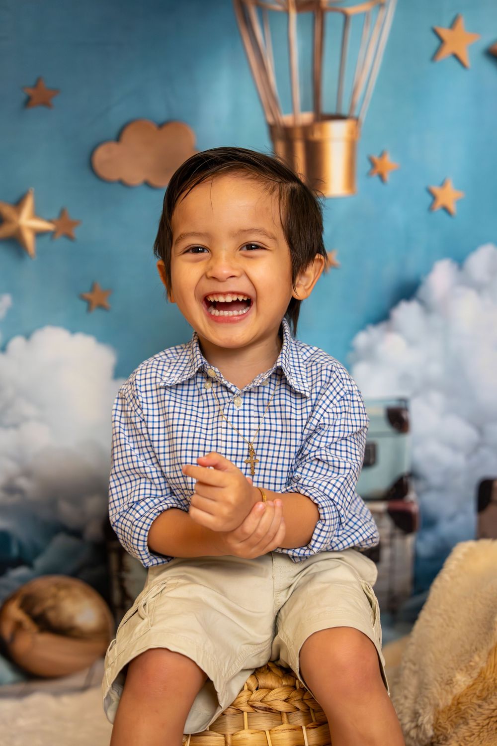 A joyful young boy in a plaid shirt laughs while sitting against a blue sky backdrop with stars and a hot air balloon.