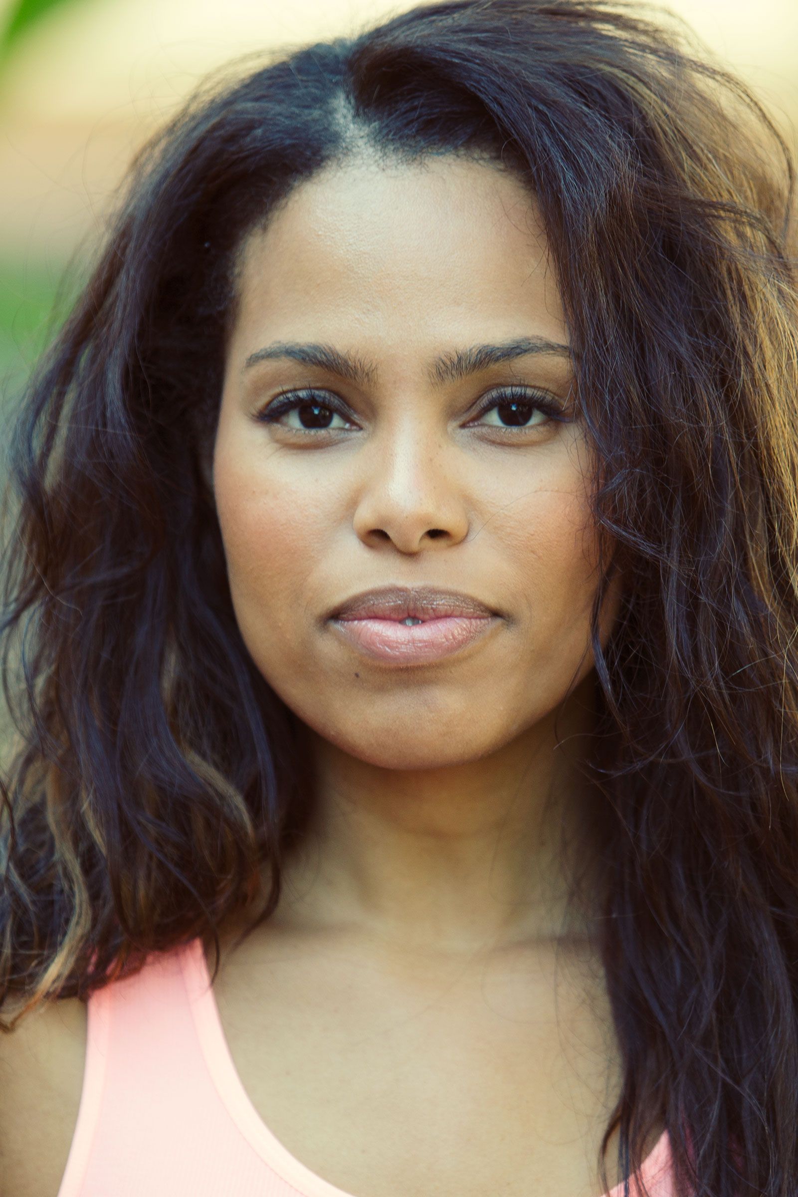 Close-up portrait of woman with wavy dark hair in pink tank top outdoors.