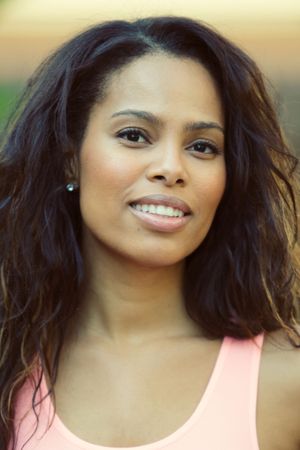 Smiling woman with wavy dark hair wearing a pink tank top outdoors.