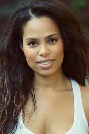 Portrait of woman with curly dark hair in white tank top outdoors.