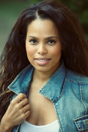 Woman with wavy dark hair in denim jacket smiling outdoors.