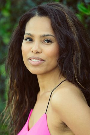 Woman with long wavy hair in pink spaghetti strap top smiling outdoors.