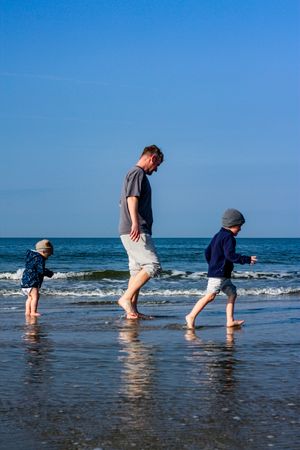 Ein Vater läuft mit seinen Kindern vor und hinter ihm am Wasser entlang.