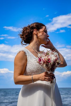 Braut mit Blumenstrauß am Ostseestrand vor blauem Himmel