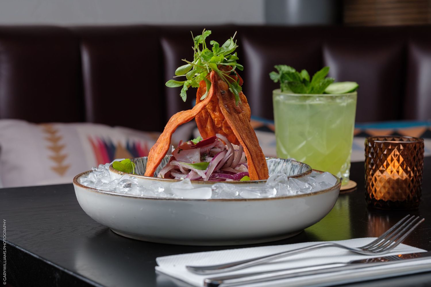 Elegant seafood dish on ice with garnish beside a fresh mojito cocktail at an upscale restaurant.