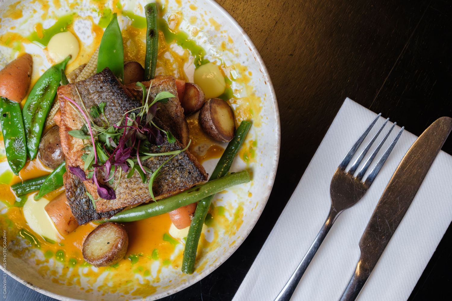 Gourmet pan-seared salmon fillet with green beans, snap peas, mushrooms, and carrots in a light broth on a white plate.