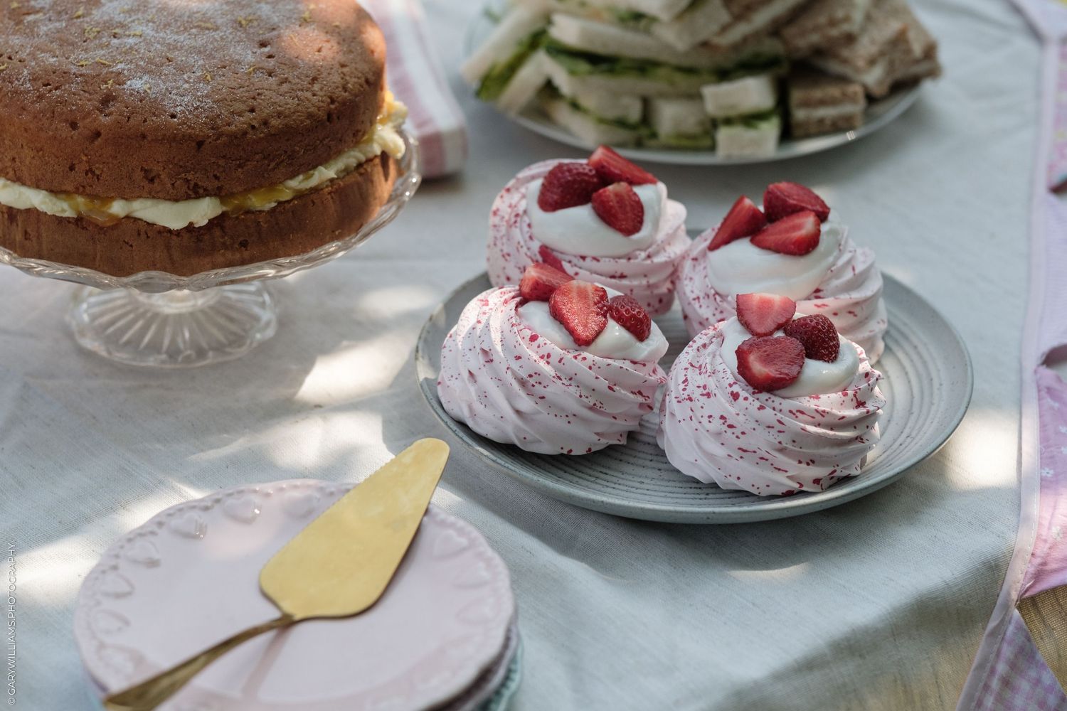 Elegant dessert table with strawberry meringues topped with fresh strawberries and a Victoria sponge cake on a glass stand.