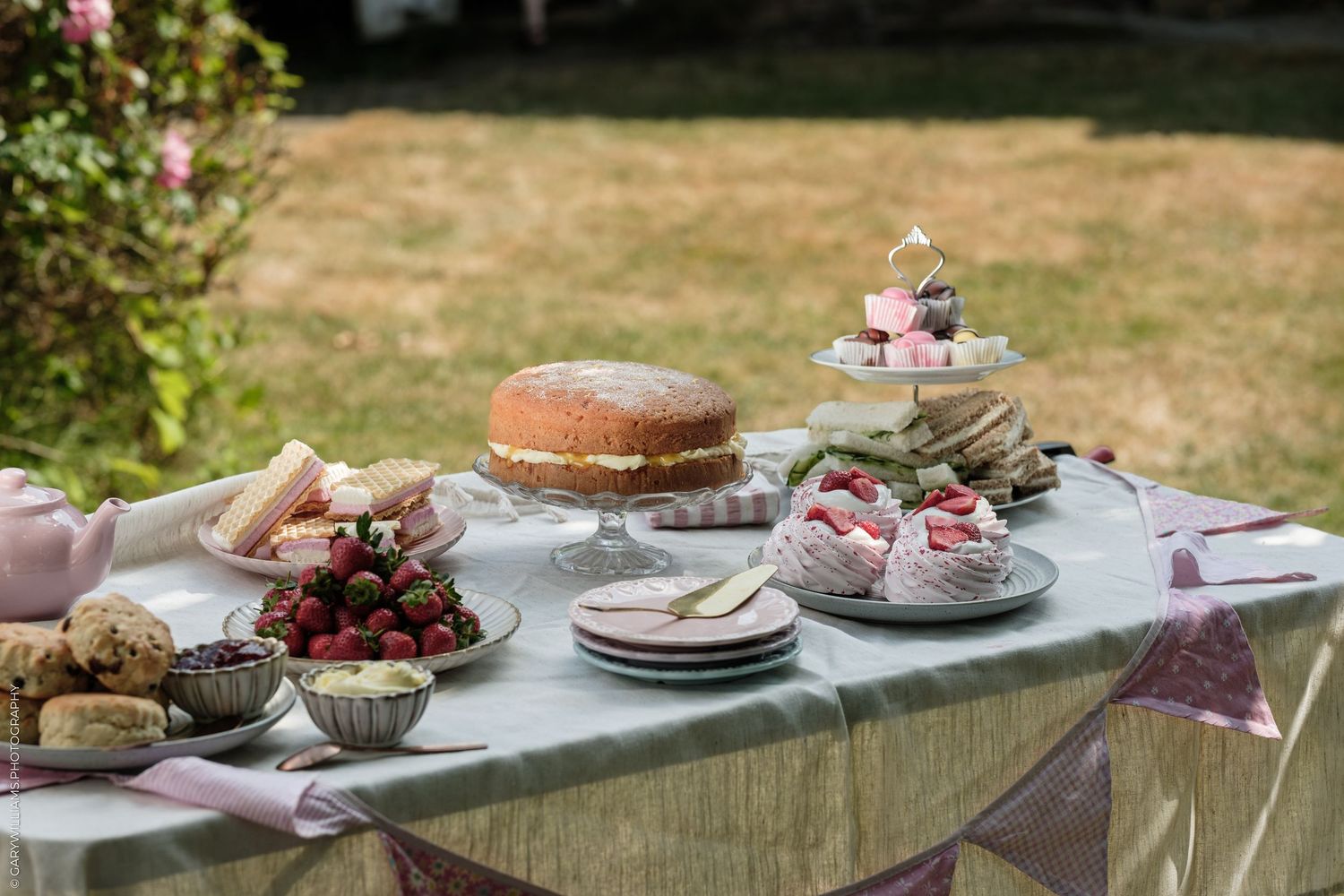 Outdoor garden party table with Victoria sponge cake, fresh strawberries, scones, and tiered cake stand with pastries.
