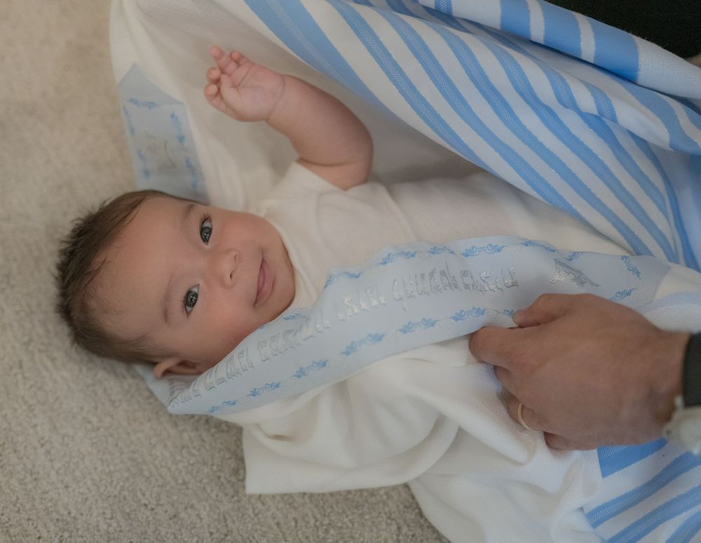 Newborn baby wrapped in a white and blue striped blanket lying on a carpet.