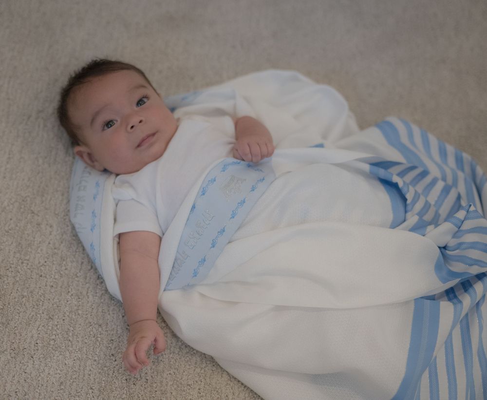 Newborn baby wrapped in a white and blue striped swaddle blanket lying on a soft carpet.