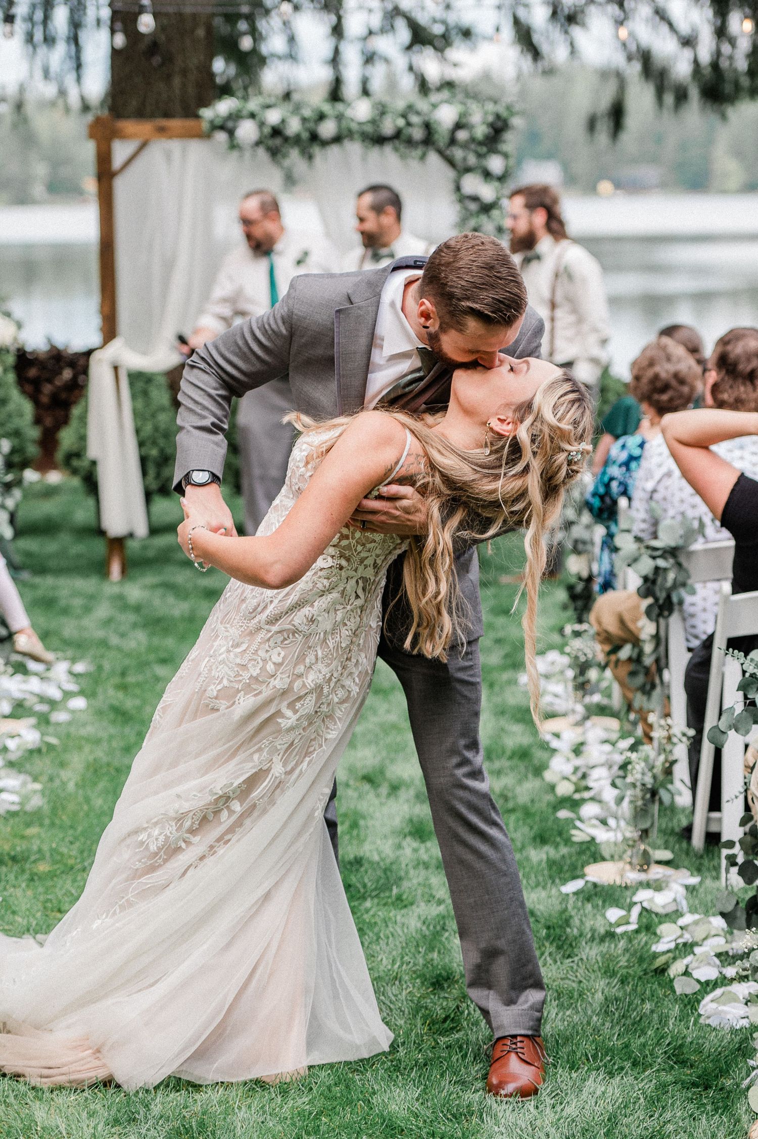 Bride and groom share a romantic dip kiss at outdoor wedding ceremony on green lawn. Photo by Bremerton Wedding Photographer