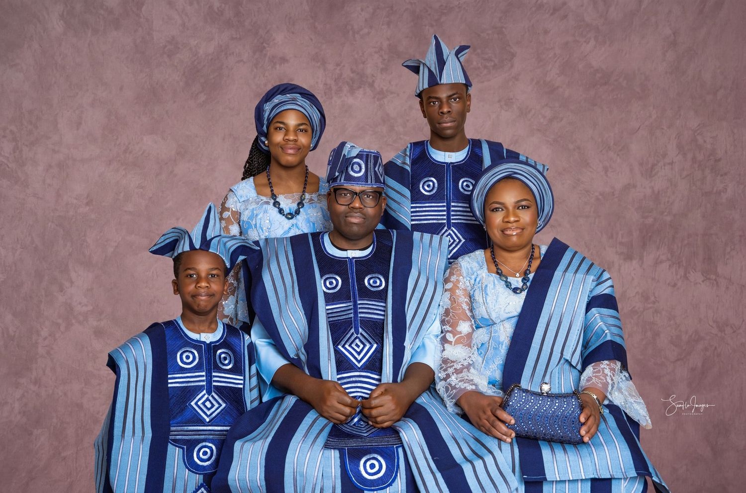 Family of five in matching blue and white traditional attire with patterned caps posing together for a formal studio portrait.