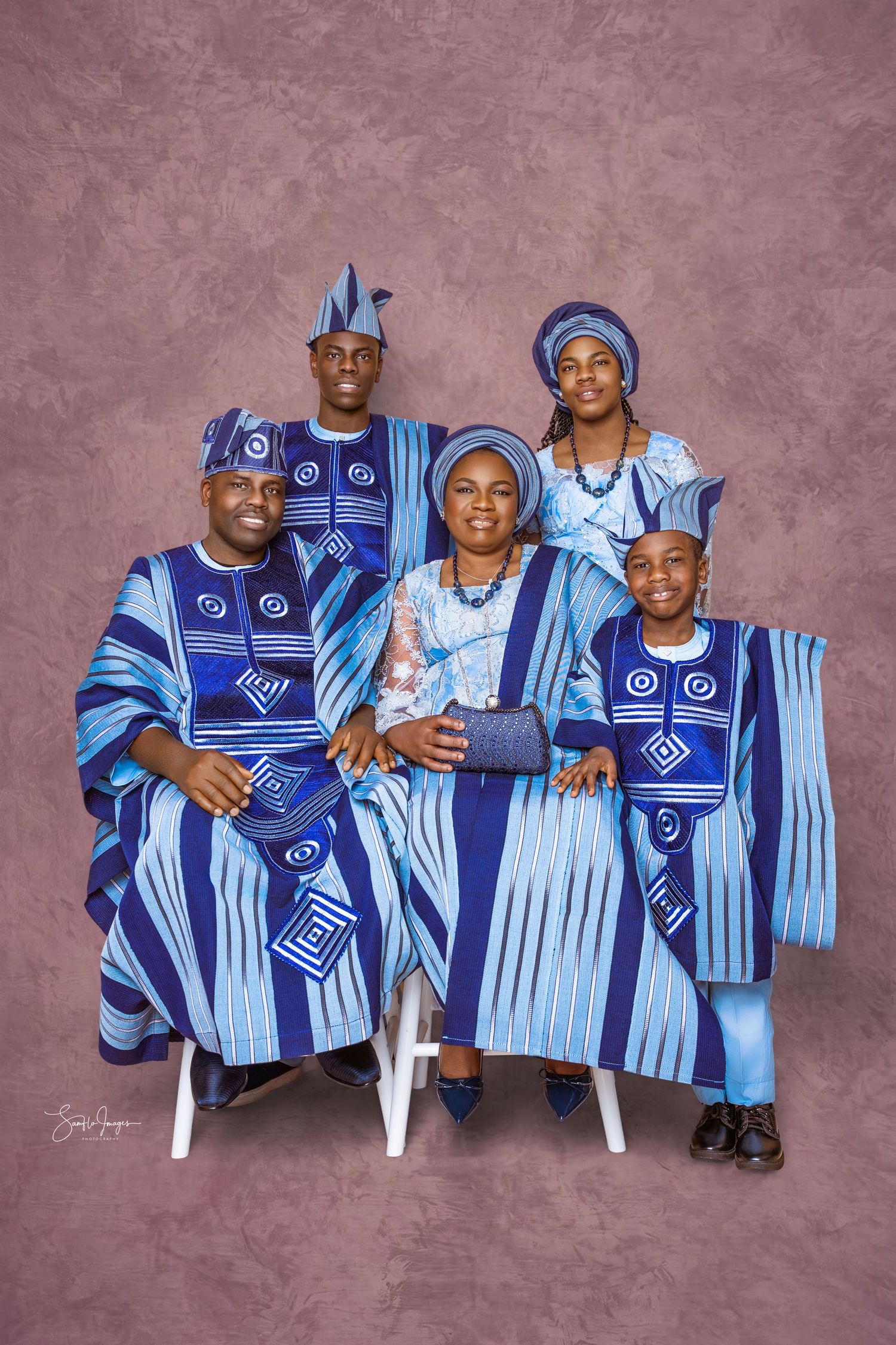 Family of four in matching blue and white patterned traditional Nigerian attire with caps posing together in a studio portrait.