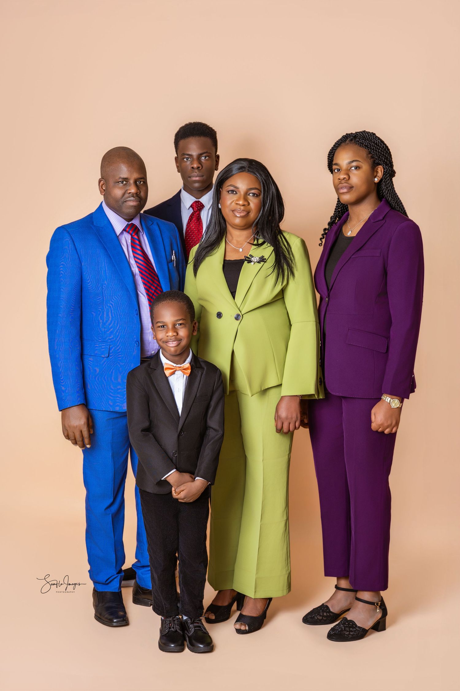Family of five in colorful formal suits, blue, lime green and purple, posing together in a studio portrait against a peach backdrop.
