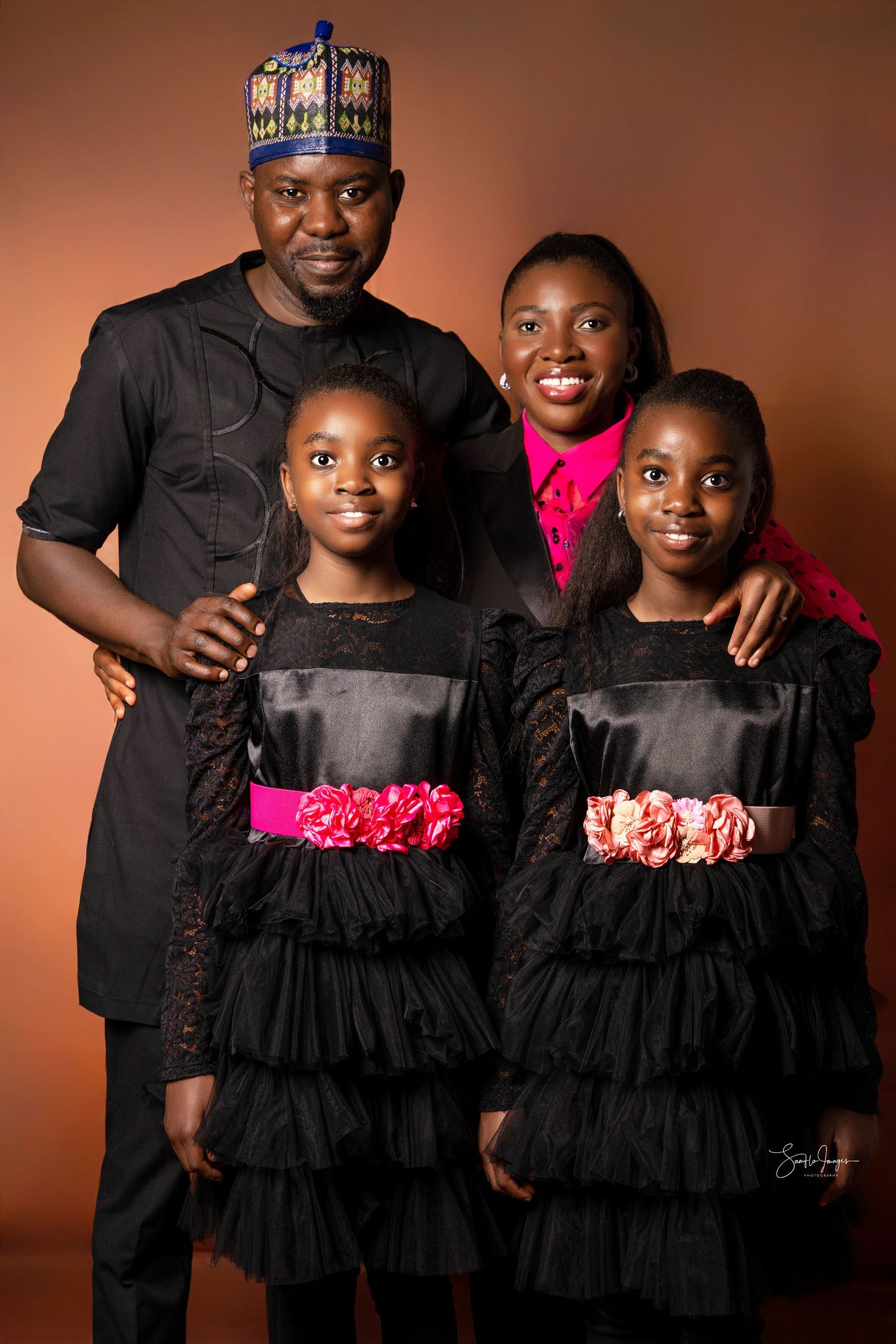 Family of four posing in matching black outfits with pink accents in a professional studio portrait photo.