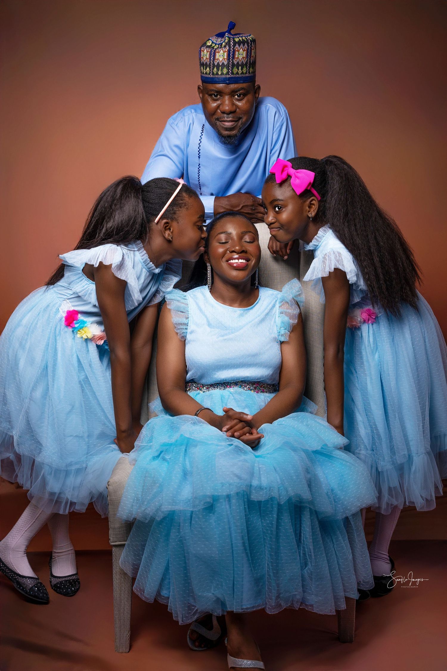 A joyful African family portrait with a father, mother, and two daughters in matching blue outfits for a studio photo.