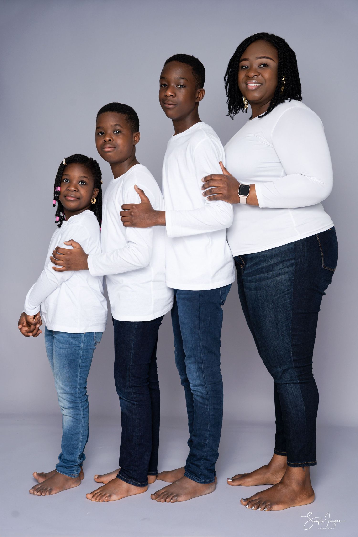 Family of four in matching white shirts and jeans pose together barefoot in a studio portrait.