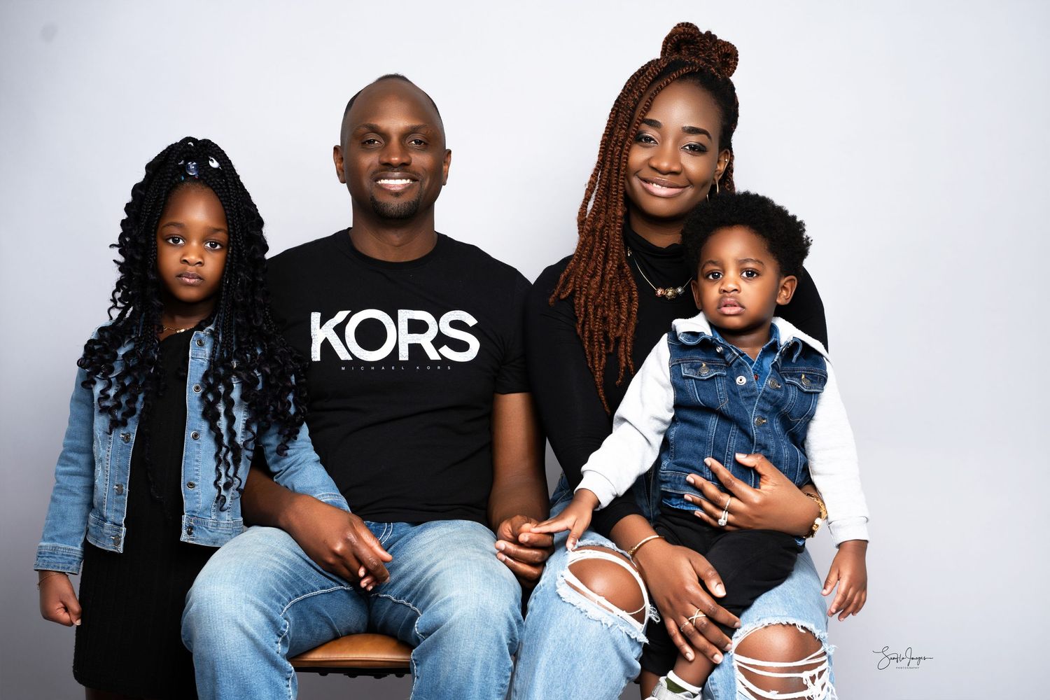A happy family of four poses for a professional studio portrait, wearing casual denim and graphic tees.