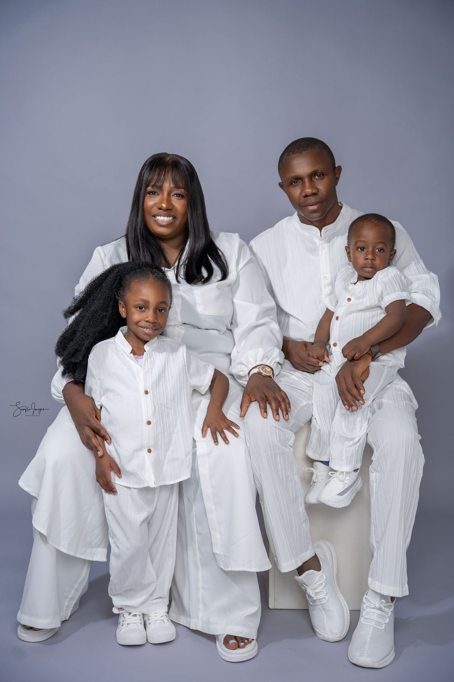 A joyful family of four wearing matching white outfits poses together for a studio portrait photo.