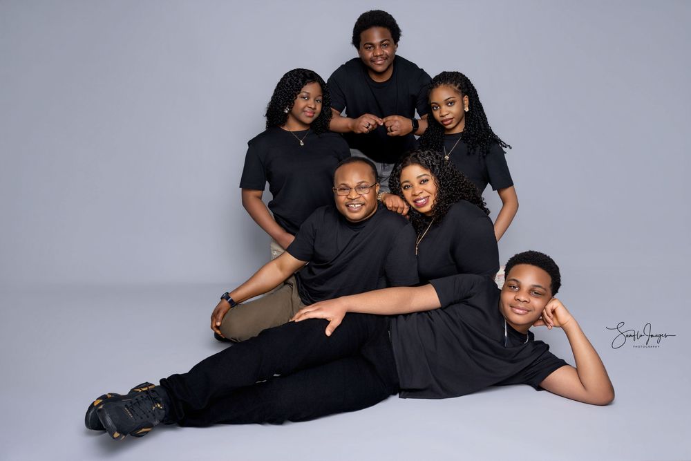 Family of six posing together in matching black outfits for a professional studio portrait photo.