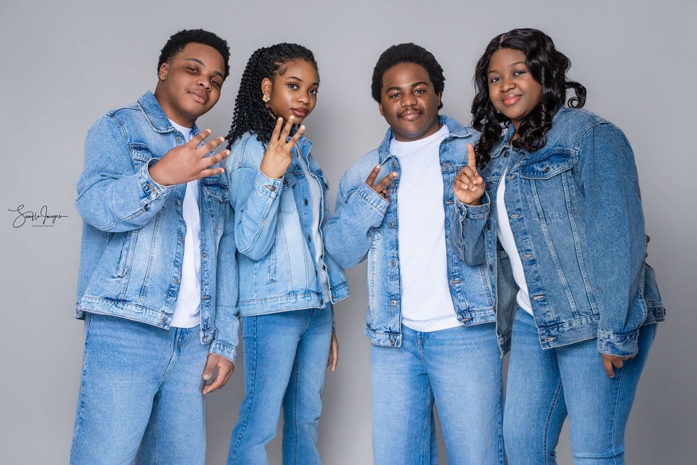 Four people in matching denim outfits posing together for a coordinated family photo shoot against a gray background.