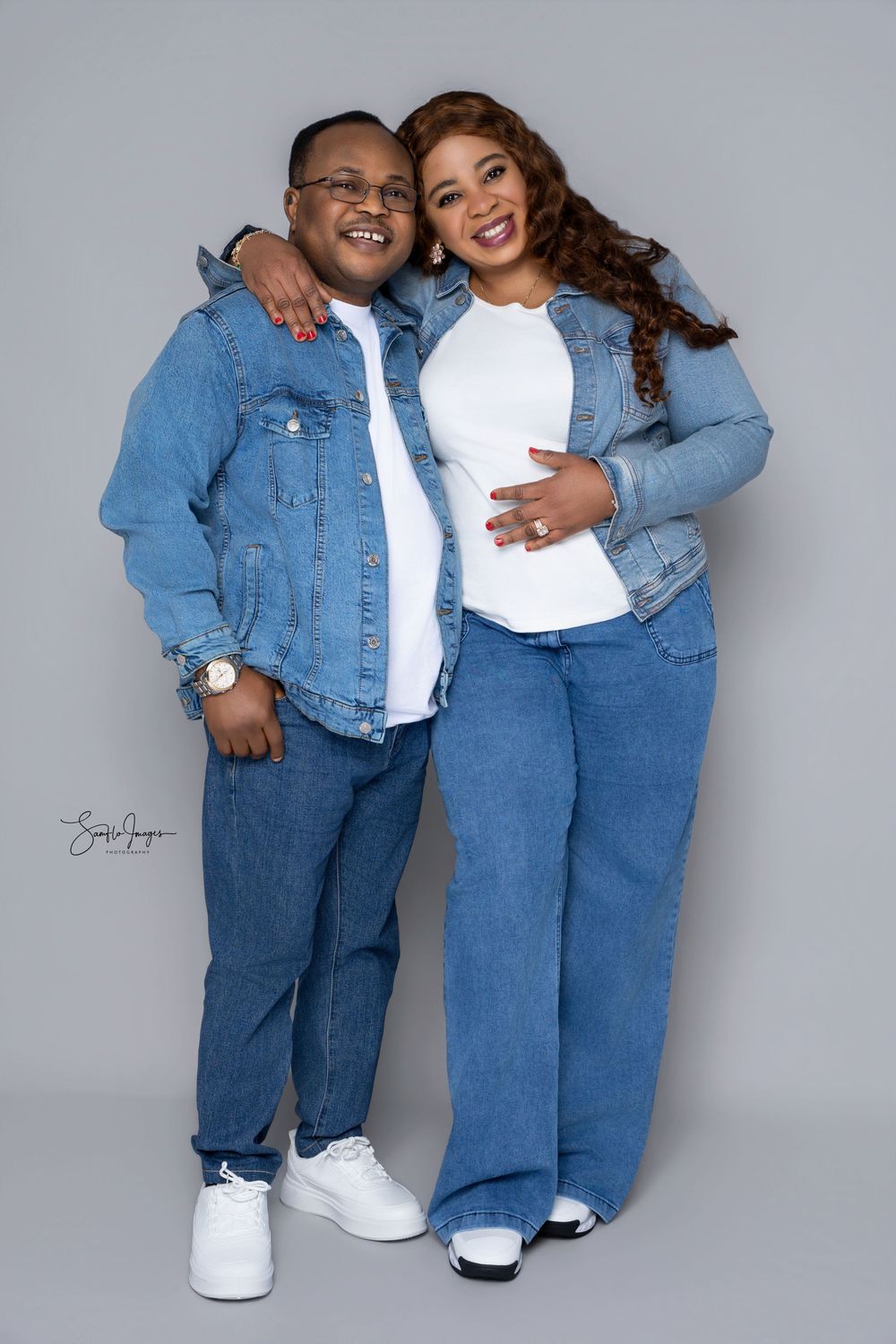Two people in matching denim outfits and white tops pose together smiling in a professional studio photo shoot.