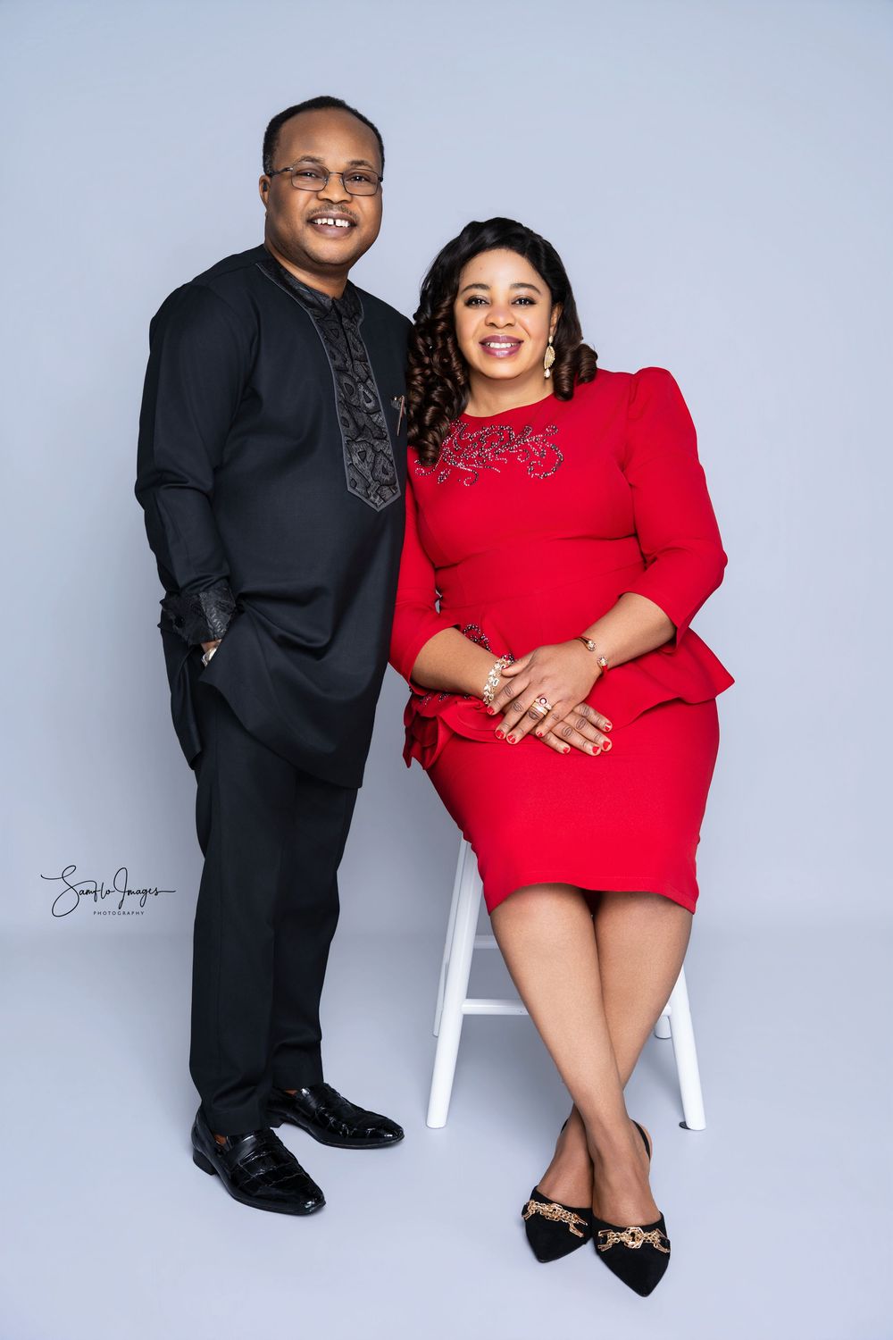 A man in black suit and woman in red dress pose together for a professional portrait photo.