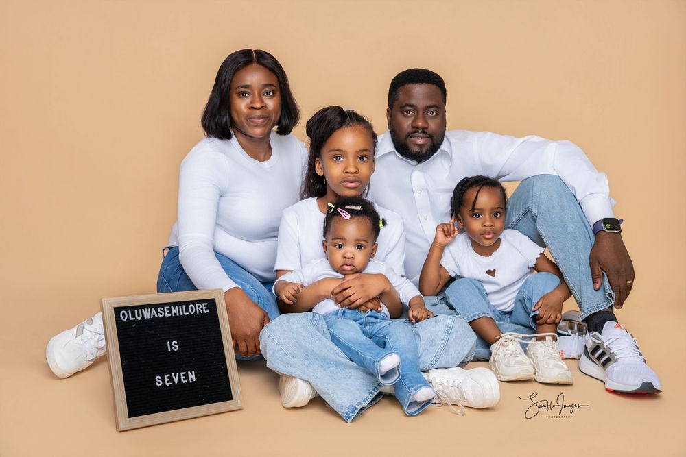 Family of five posing together for a professional portrait with a letter board reading Oluwasenilore is Seven.