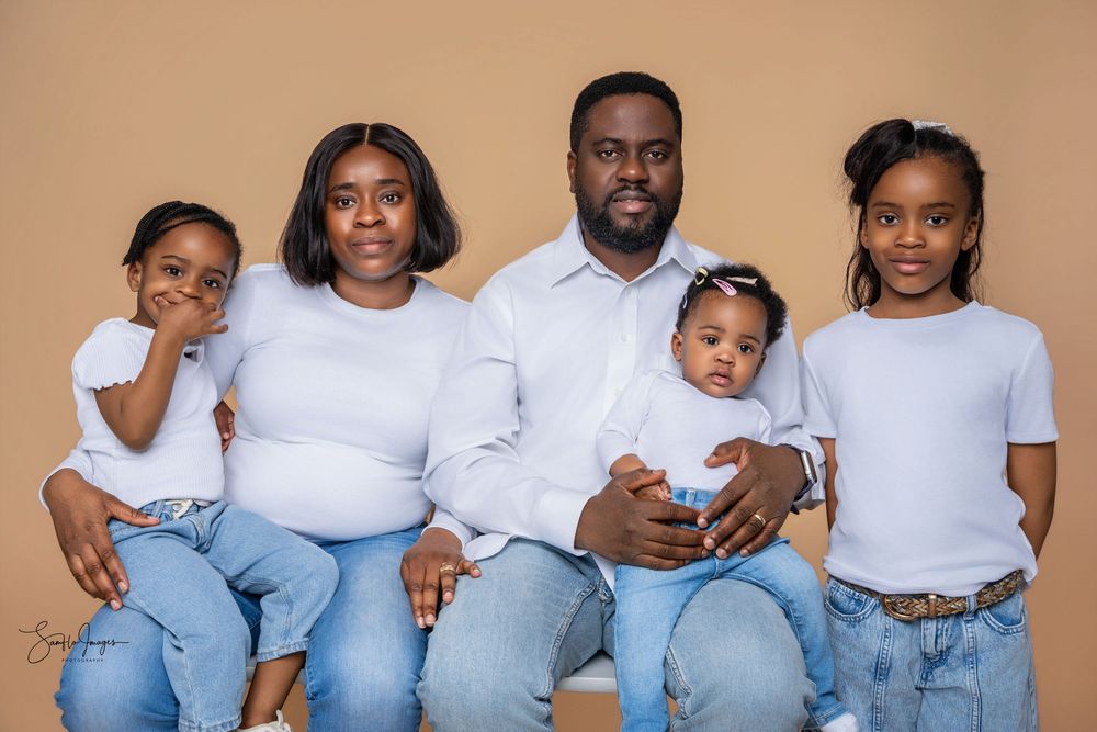 Family of five in matching white tops and jeans posing together for a professional portrait photo.