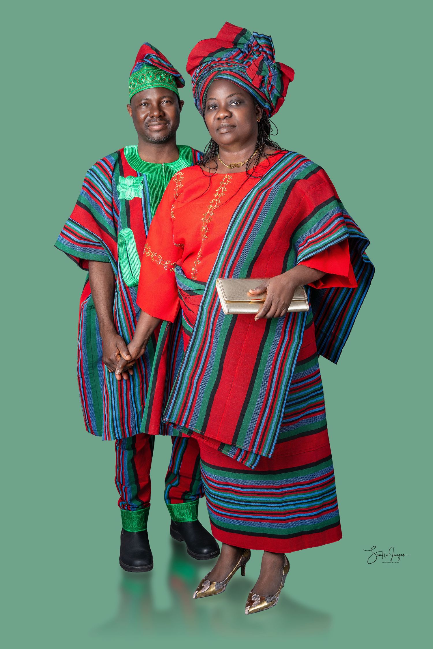 Two people in vibrant red and green African traditional attire pose together for a formal portrait photo.