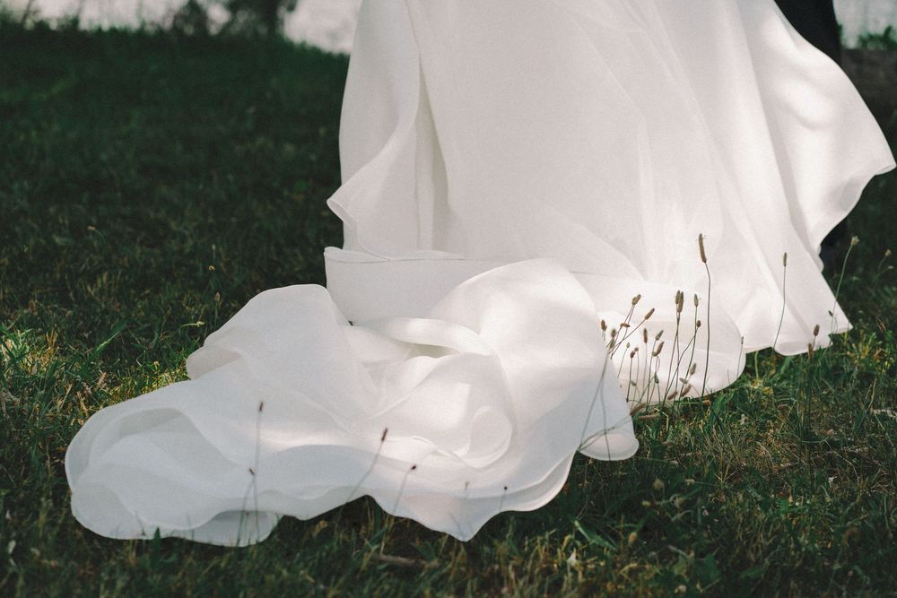White wedding dress train flowing gracefully on green grass outdoors.