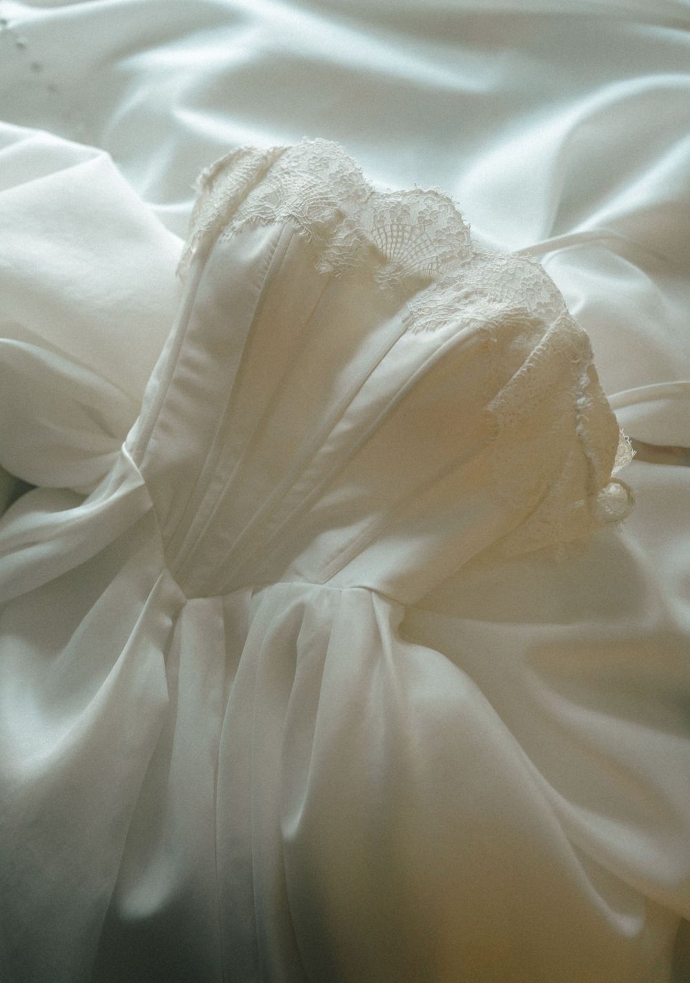 Close-up of an elegant white wedding dress with delicate lace bodice and flowing satin fabric details.